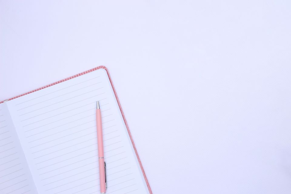 An open notebook, pencil and coffee cup on a wooden desk.