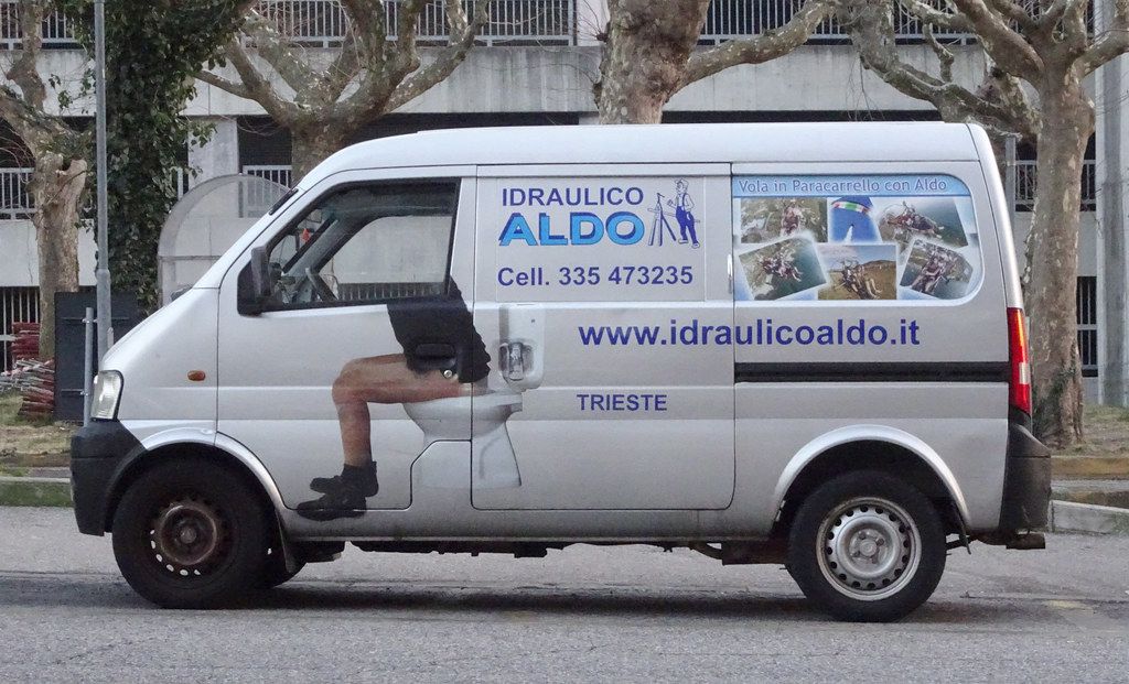 A plumber standing beside a work van outside a brick terraced house.