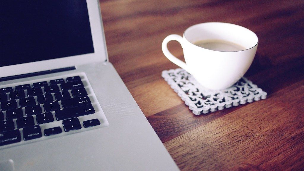 An open laptop beside a notebook and coffee on a wooden desk.