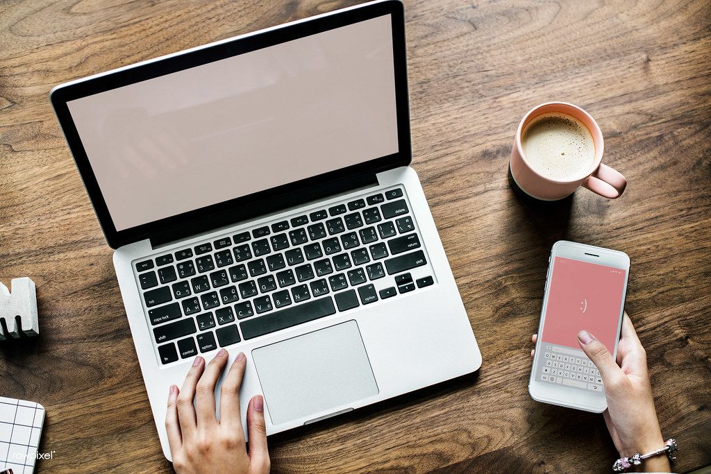 A café owner sitting at a wooden table with an open laptop and a cup of coffee.